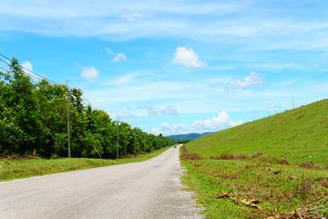 Fototapeta na wymiar empty asphalt country road along the wall of dam with green grass and blue sky with clouds and mountain background in countryside
