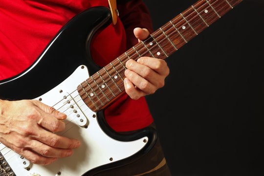 Musician put fingers for chords on electric guitar on the black background
