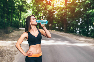 Young fitness girl drinking water in the park