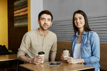 Two beautiful young students sitting in cafeteria, drinking cocoa, smiling, looking in camera posing for university newspaper article