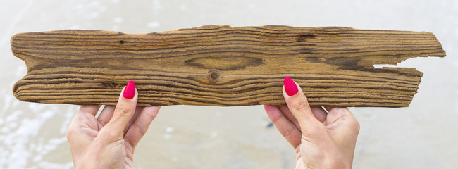 Wooden plaque in the hands on beach. Place empty for text. Sales and advertising concept. Travel...