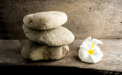 White flower and leafs with big and tiny stone and towel on wood table for health spa advertisement and presentation