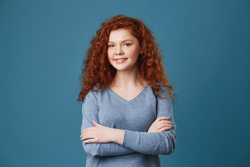 Close up portrait of beautiful student with redhead hair and freckles in grey shirt crossing hands,...