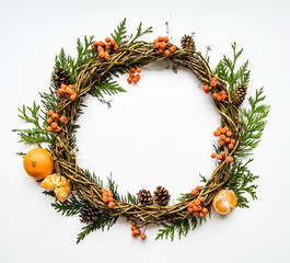 Festive wreath of vines with tangerines, thuja branches, rowanberries and cones. Flat lay, top view