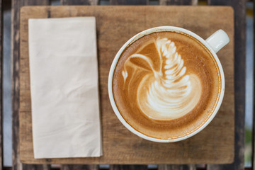 A cup of coffee with latte art in a swan shape on wooden tray.
