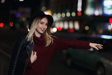 Young beautiful girl catches a taxi in the city street at night