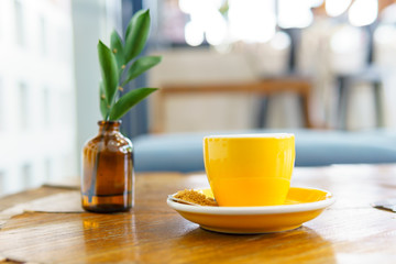 ristretto or espresso coffee shot in yellow cup with  spoon of brown sugar and small plant in brown bottle on old wooden table.