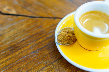 ristretto or espresso coffee shot in yellow cup with  spoon of brown sugar on old wooden table. copy space for text.