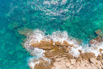 A bird's-eye view of how turquoise waves beat about sea cliffs in Montenegro