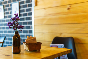close up of purple flower bouquet in brown bottle with bucket of tissues.