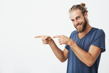 Joyful mature guy with beard posing for article in university newspaper pointing aside with fingers on both hands and smiling.