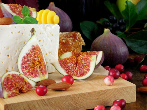 Cheese made of sheep milk and slices of figs on a wooden board surrounded by cranberries and almond. Ingredients for a cheese plate