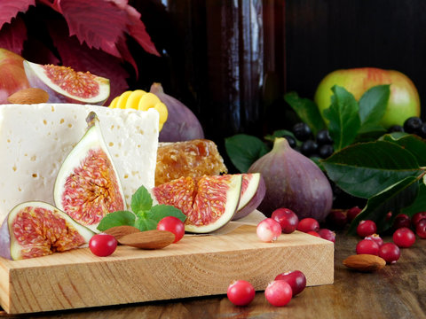 Cheese made of sheep milk and slices of figs on a wooden board surrounded by cranberries and almond. Ingredients for a cheese plate