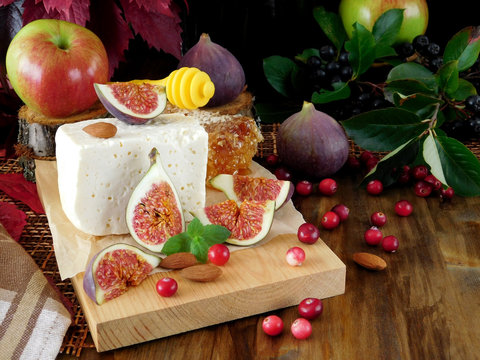 Cheese made of sheep milk and slices of figs on a wooden board surrounded by cranberries and almond. Ingredients for a cheese plate