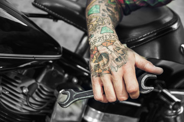 Obraz premium Wytatuowany klucz trzymający rękę obok silnika motocykla. Custom shop dla koncepcji rowerów