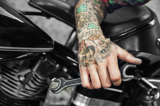 Fototapeta Tattooed hand holding wrench next to motorcycle engine. Custom shop for bikes concept