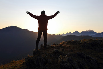 Fototapeta na wymiar tourist with arms raised standing on the mountain at dawn