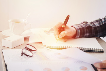 Naklejka premium Hands of businessman writing something on notebook paper, and business finance report document blurred on table