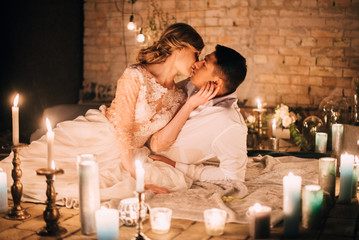 beautiful couple embracing and lying on a blanket in a dark room, surrounded by burning candles