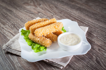 fish sticks with tartar sauce, on a wooden board with greens