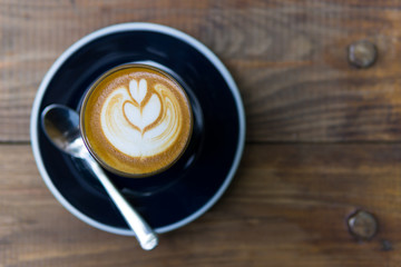 Hot latte coffee in dark blue cup with spoon of the vintage wooden table.
