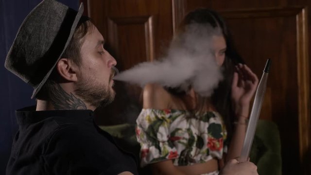 The guy with the girl is sitting on the sofa in the cafe and smoking a hookah