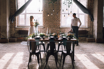 beautiful bride and groom in room with decorated table with flowers, candles and light bulbs