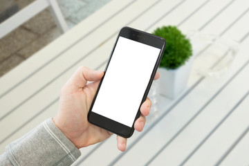 Mobile phone showcase. Black smart phone mockup. White wooden desk with plant in background.