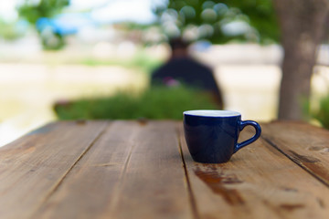espresso or ristretto coffee in dark blue cup on the wooden table near the river in sunny day.