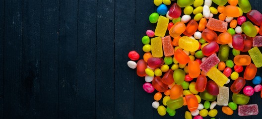 Colored candies, sweets and lollipops. On a black wooden background. Top view. Free space.