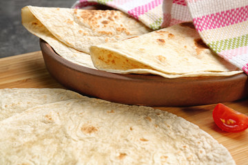 Wooden board with delicious tortillas on table, closeup