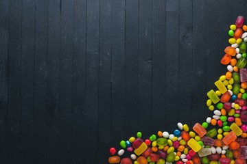 Fototapeta premium Colored candies, sweets and lollipops. On a black wooden background. Top view. Free space.