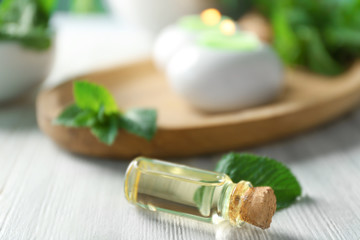 Bottle of essential oil and leaves of mint on wooden table