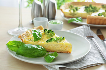 Plate with piece of tasty broccoli quiche on table