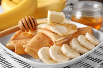 Delicious pancakes with honey, banana and butter on plate