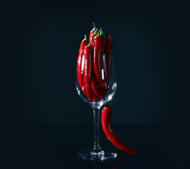 Glass with red chili peppers on black background