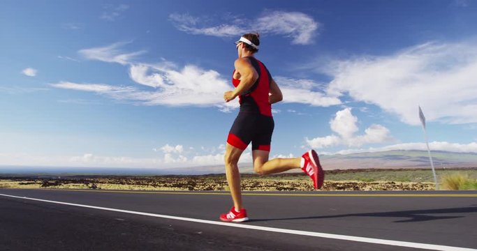 Triathlete man running in triathlon suit training for ironman. Male runner exercising running on road on Big Island Hawaii, USA. RED EPIC SLOW MOTION.