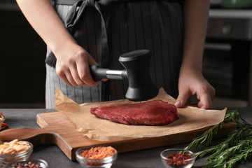 Femme battant un steak cru avec un maillet à viande dans la cuisine