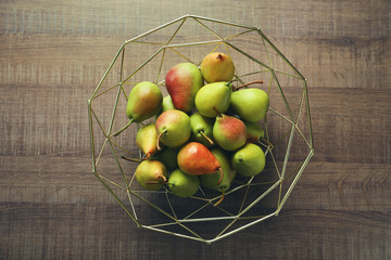 Ripe pears in metal fruit bowl on wooden table