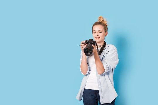 Young blonde photographer holds a camera and looks at the photo she made