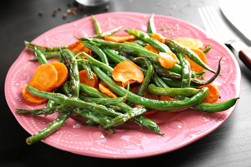 Pink plate with delicious green beans and carrot slices on table