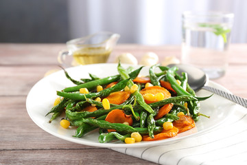 Plate with delicious green beans, corn and carrot slices on table