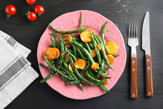 Pink plate with delicious green beans and carrot slices on table