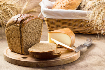 Bread and cheese sliced for sandwiches amid the loaves in a wicker basket with ears of wheat