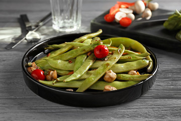 Black plate with delicious green beans, mushrooms and cherry tomatoes on table