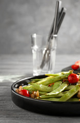 Black plate with delicious green beans, mushrooms and cherry tomatoes on table