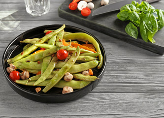 Black plate with delicious green beans, mushrooms and cherry tomatoes on table