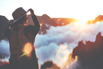 Smiling happy girl wearing hat and backpack enjoying the sunset and clouds in the mountains.