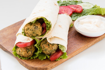 Falafel and fresh vegetables rolled in pita bread on wooden board