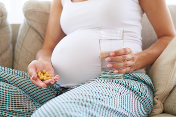 Pregnant woman hand with glass of water and pills